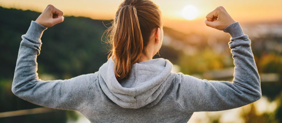 Woman flexing biceps gazing sunrise symbolizing motivation empowerment (1)